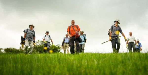 Ramblers volunteers carrying maintenance tools across a field